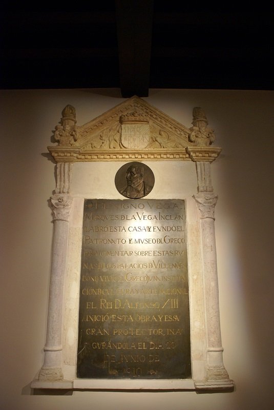 Placa conmemorativa con la leyenda:-Benigno Vega, Marqués de la Vega Inclán, labró esta casa y fundó el Patronato del Museo del Greco para cimentar sobre estas ruinas de los palacios de Villena (en donde vivió el Greco) una institución de cultura y arte nacional. El rey D. Alfonso XIII, inició esta obra y es su protector, inaugurándola el día 20 de junio de 1910-. La placa se encuentra situada en el distribuidor de la casa. Casa del Greco
